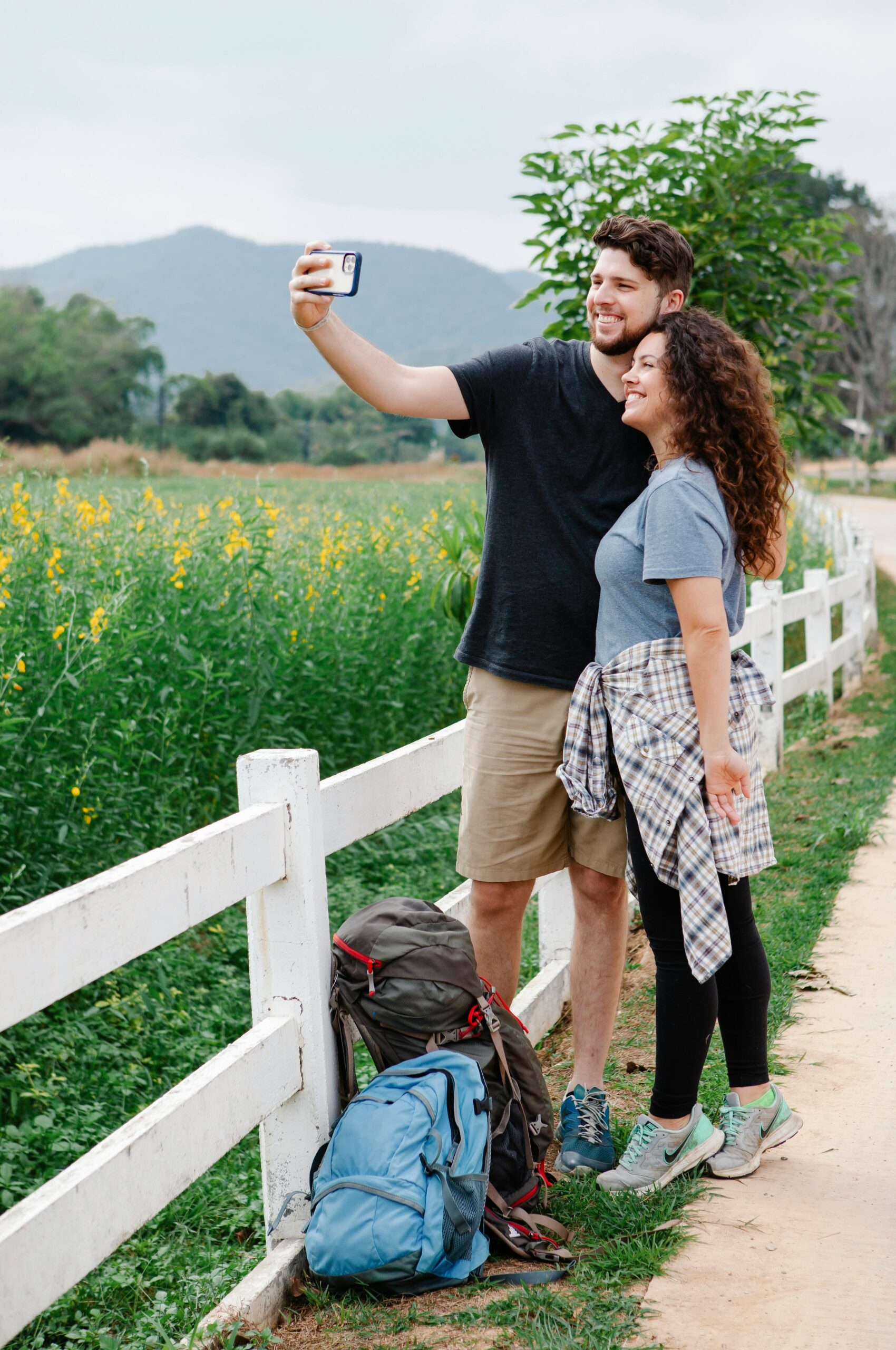 Happy couple taking selfie standing near green meadow in mountainous countryside